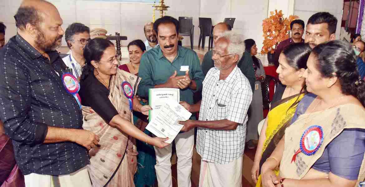 അദാലത്തില്‍ പങ്കെടുത്ത റിട്ടയേര്‍ഡ് കെ. എസ്. ആര്‍. ടി. സി ഉദ്യോഗസ്ഥന്‍  പി. എസ്. ജോണിന്  മന്ത്രി വീണാ ജോര്‍ജ്ജ് ആധാരം രജിസ്റ്റര്‍ ചെയ്ത രേഖ കൈമാറുന്നു, മന്ത്രി പി. രാജീവ് സമീപം